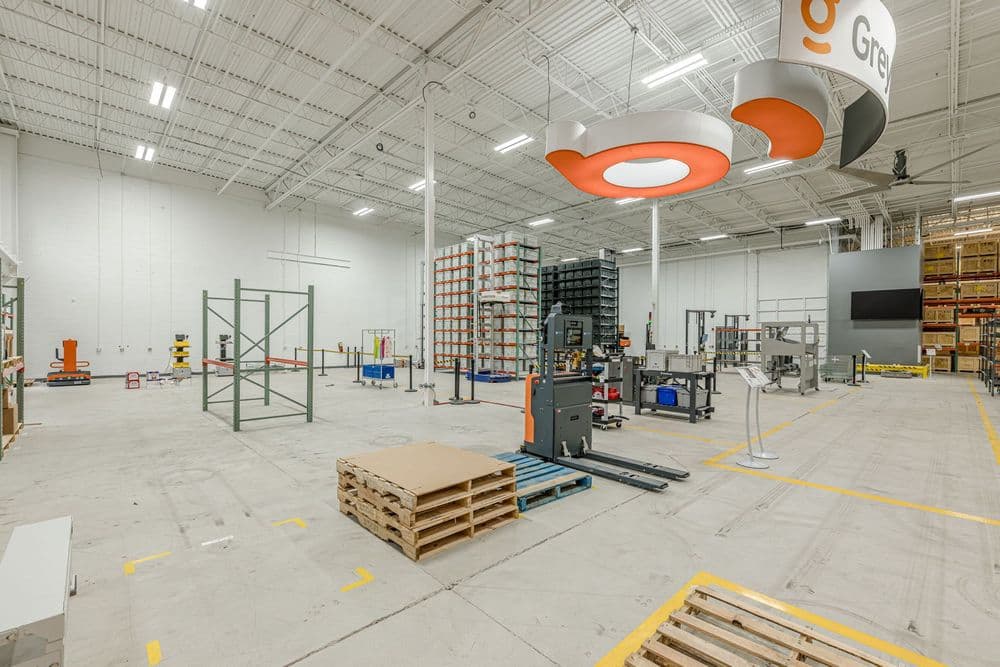 Spacious warehouse interior with storage racks, equipment, and bright overhead signage.